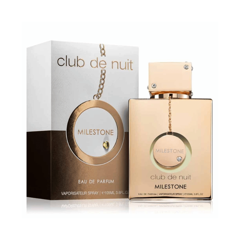 A product shot of the ARMAF Club de Nuit Milestone perfume. The gold-toned glass bottle with a decorative chain and a clear jewel is next to its matching white and gold box.