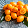 A pile of small orange kumquats on a rustic wooden surface, with two fruits sliced in half.